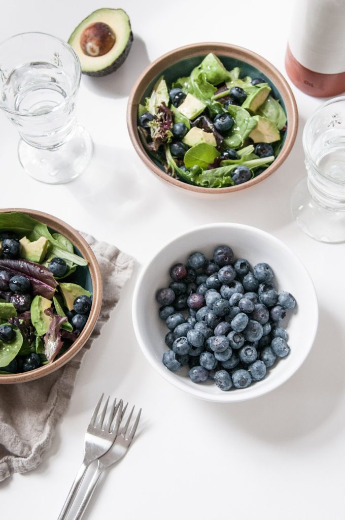 An image of two small brown ceramic bowls containing Superfood Avocado Blueberry Salad. There is also a small white ceramic bowl filled with fresh blueberries.