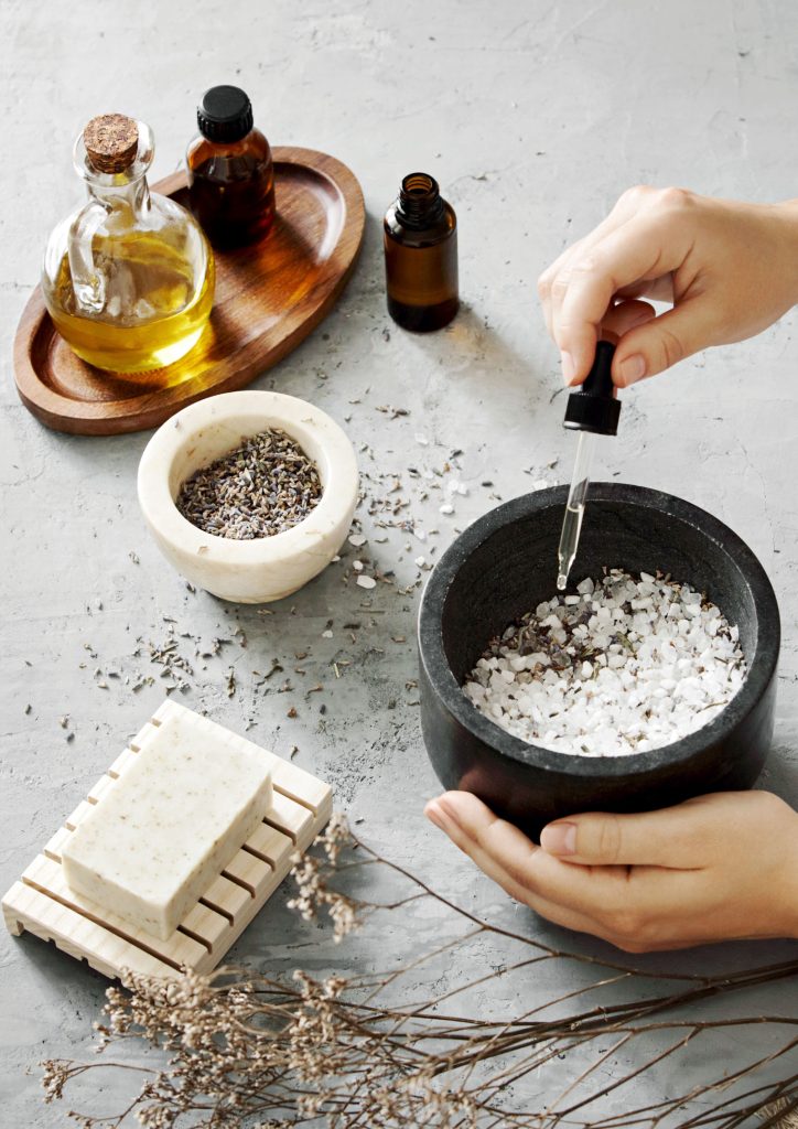 A photograph showing a person (not in sight) adding essential oils to coarse bath salts in a small black granite bowl.