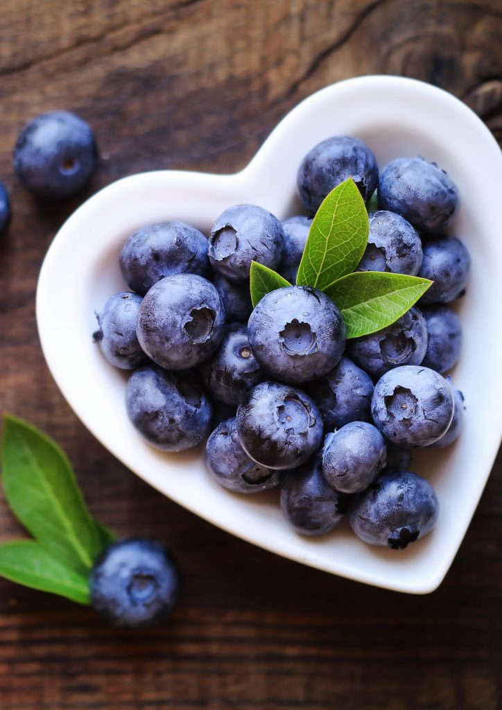 Image of a small heart-shaped white ceramic bowl containing blueberries.