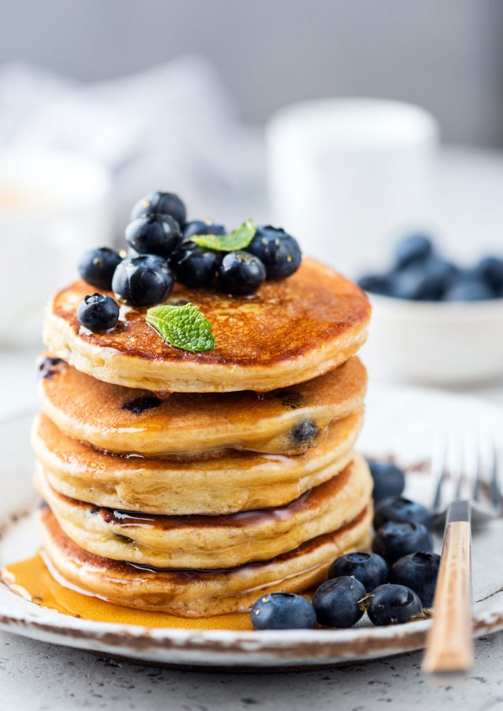Image of a stack of blueberry pancakes drizzled in maple syrup.