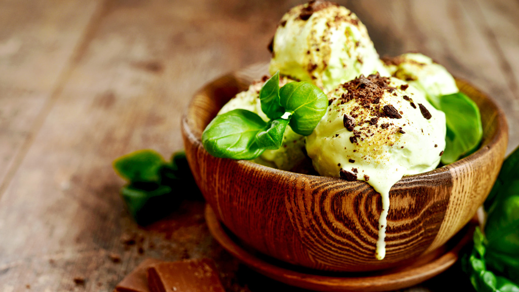 An image of a wooden round bowl containing basil ice cream topped with grated chocolate. summertime.