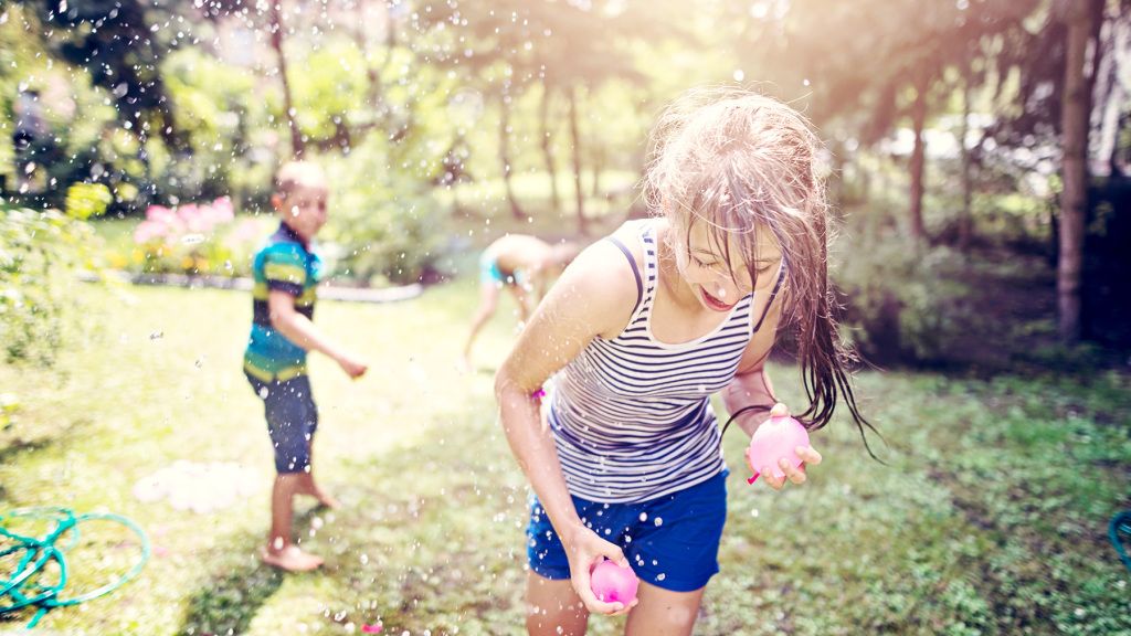An image of two children playing with water balloons in a garden during a summer's hot day. Summertime.
