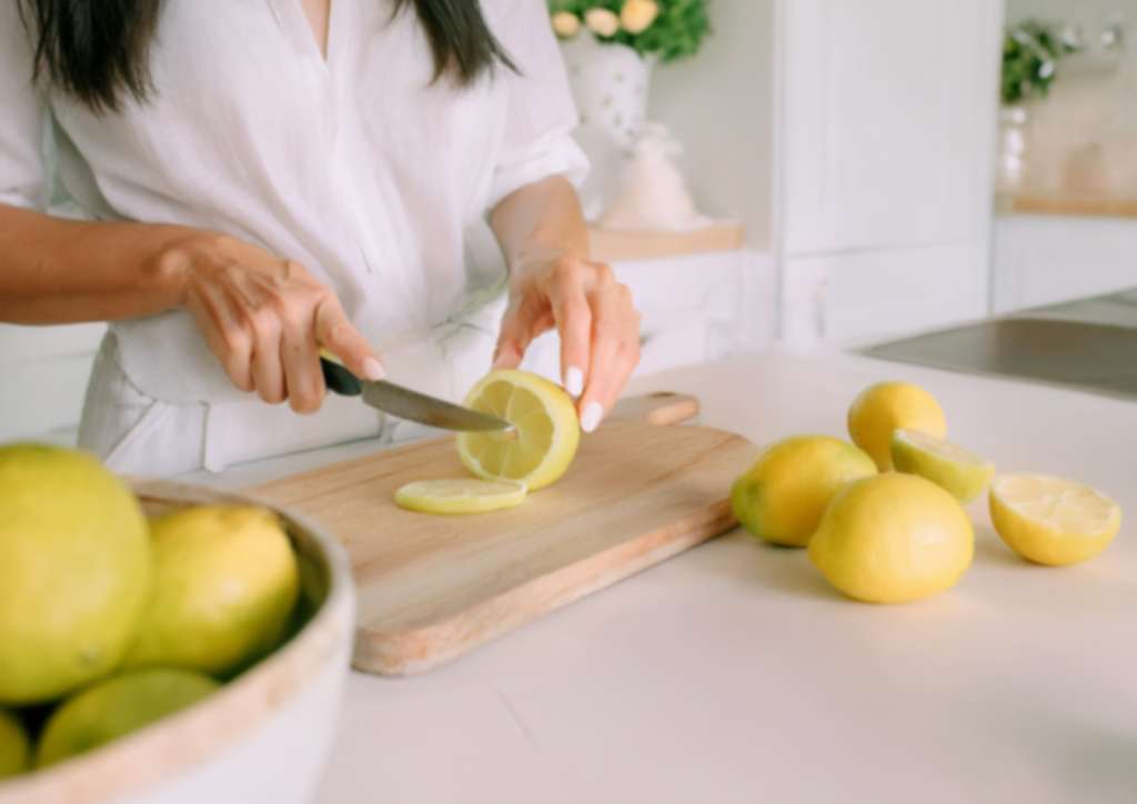 An image of a woman dressed in white cutting lemons in a white kitchen.
