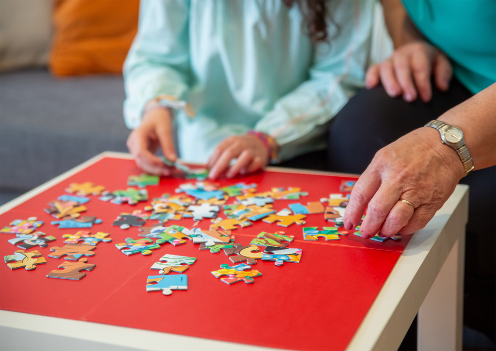 Image of an unseen child and older person piecing together a jigsaw puzzle.