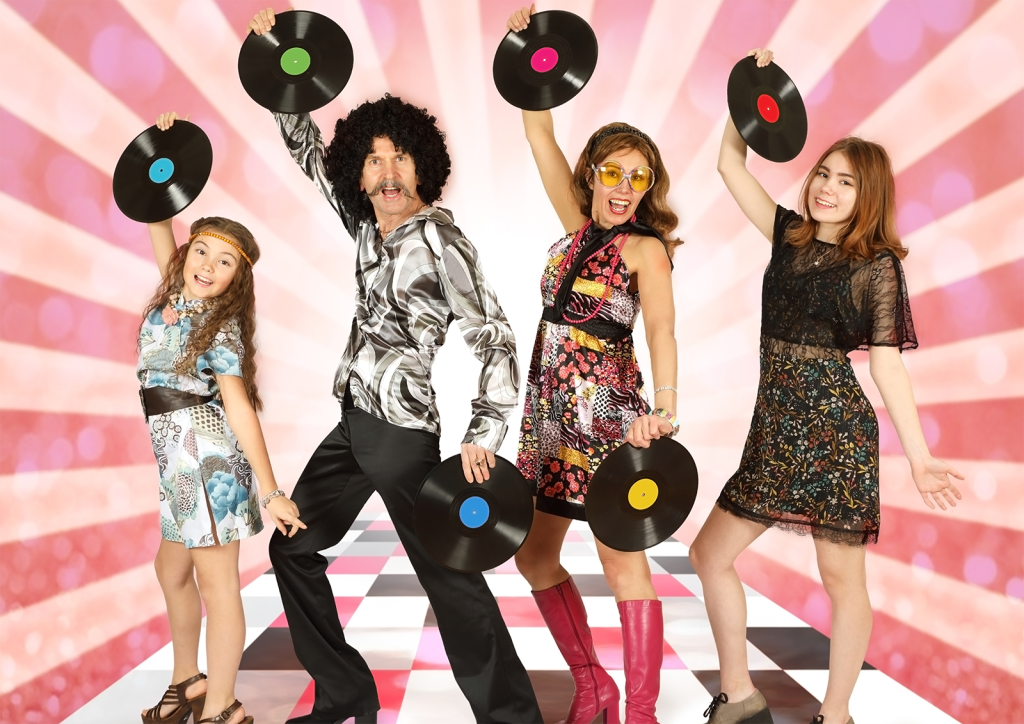 Image of a 1970s themed event. People in the image are wearing fashions from the 1970s and are holding up vinyl albums. They are standing in front of a pink and white "sunray" retro backdrop.