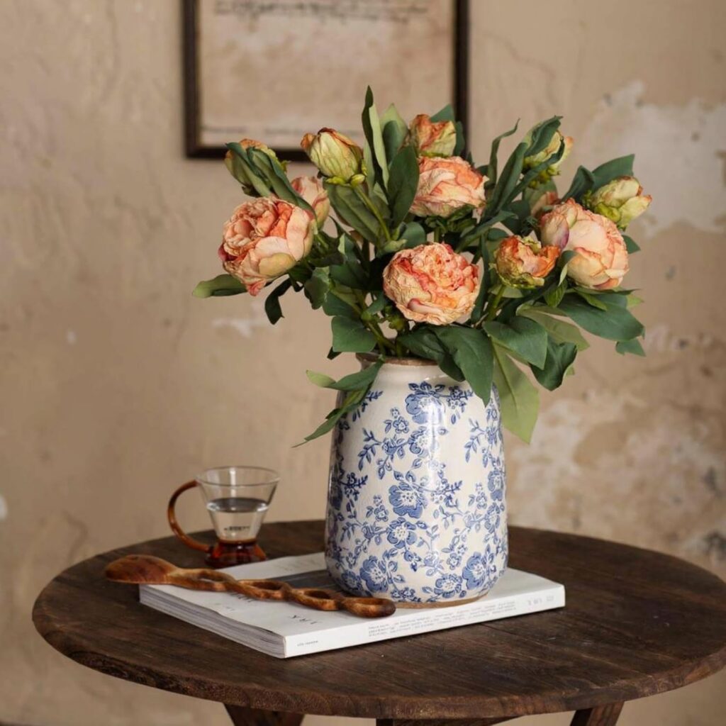 An image of a blue and white ceramic chinoiserie vase filled with pink blooms. The vase sits on a small round dark wood table. The vase is available to buy from Amazon.