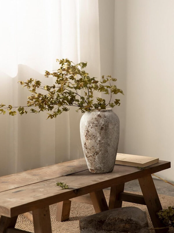 Rustic tall ceramic vase with mottled handmade glaze finish styled on a wooden bench with foliage branches